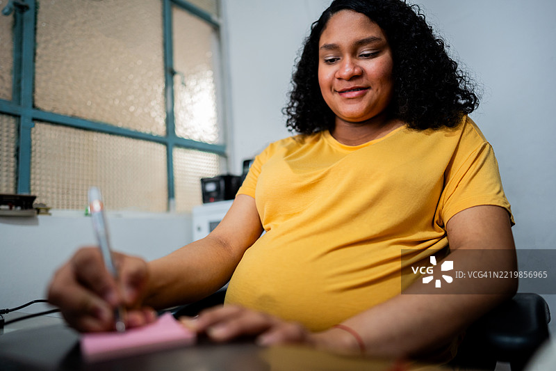 年轻的孕妇在办公室记笔记图片素材