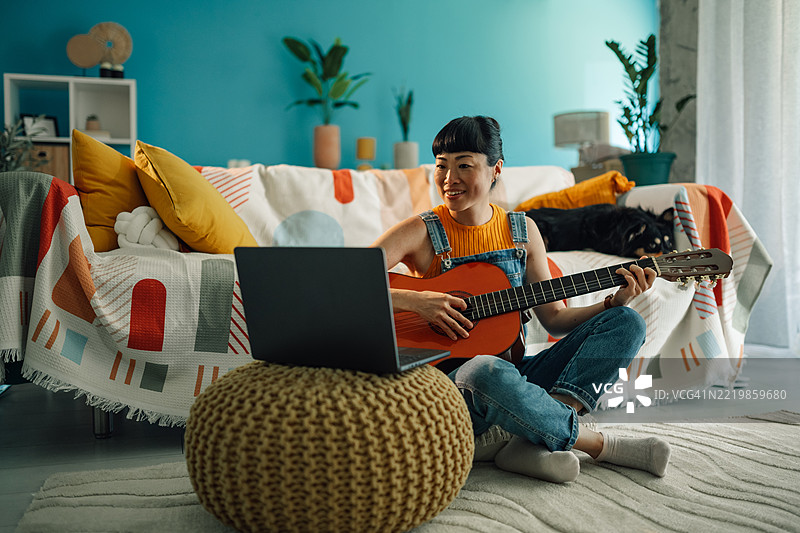年轻女性在家中弹吉他并跟随在线音乐课程图片素材