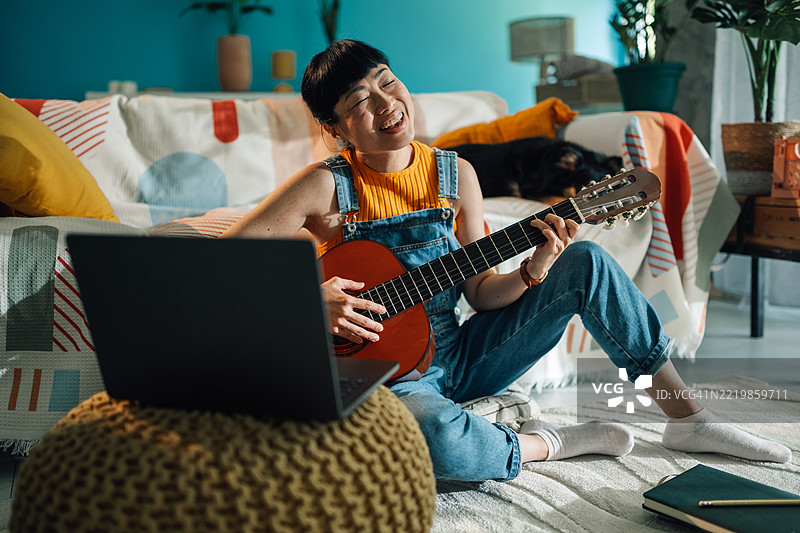 年轻的亚洲女性在家里弹吉他唱歌图片素材