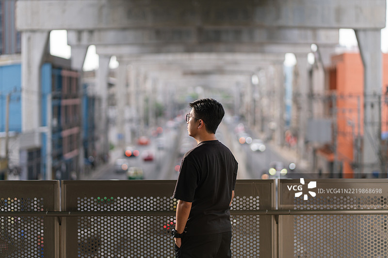 男子站在行人天桥上，俯瞰繁忙的城市街道，街道上有交通和上方的火车轨道。图片素材