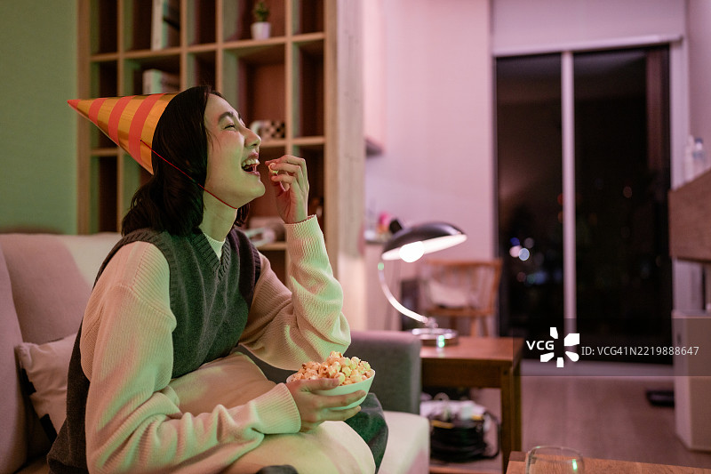 女人在沙发上放松，享受她最喜欢的节目，边吃爆米花，等待新年的倒计时。图片素材