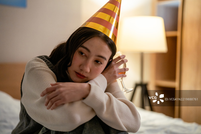 内向的女性坐在床上，手中拿着饮料，回忆过去一年和萦绕在心头的记忆。图片素材