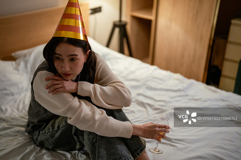 内向的女性坐在床上，手中拿着饮料，回忆过去一年和萦绕在心头的记忆。图片素材