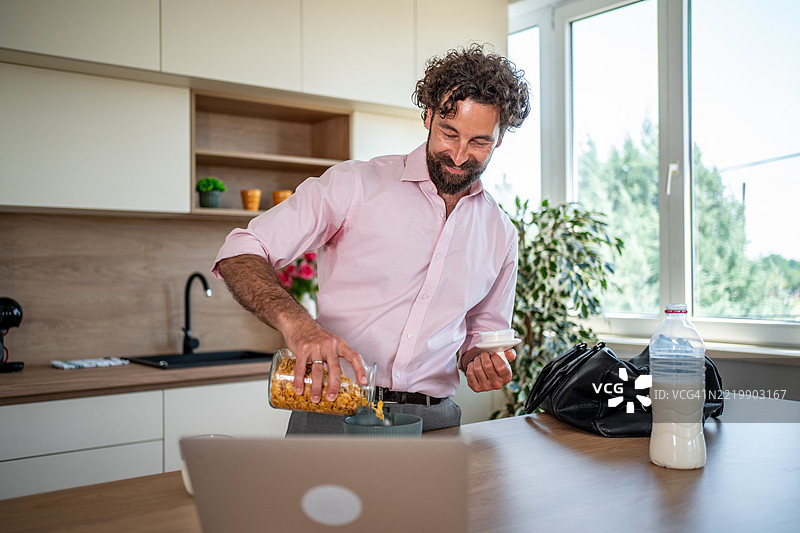商人在厨房准备早餐并使用笔记本电脑工作图片素材