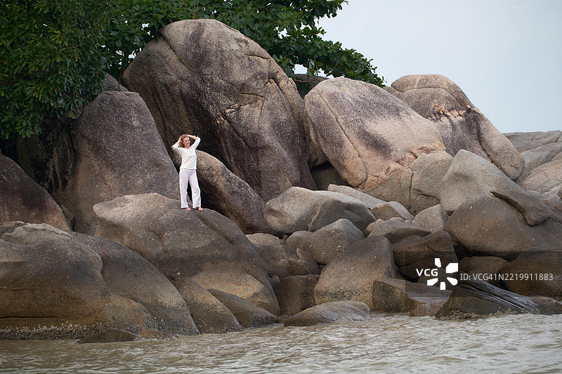 快乐的女人在夏日海边的岩石上享受时光。图片素材