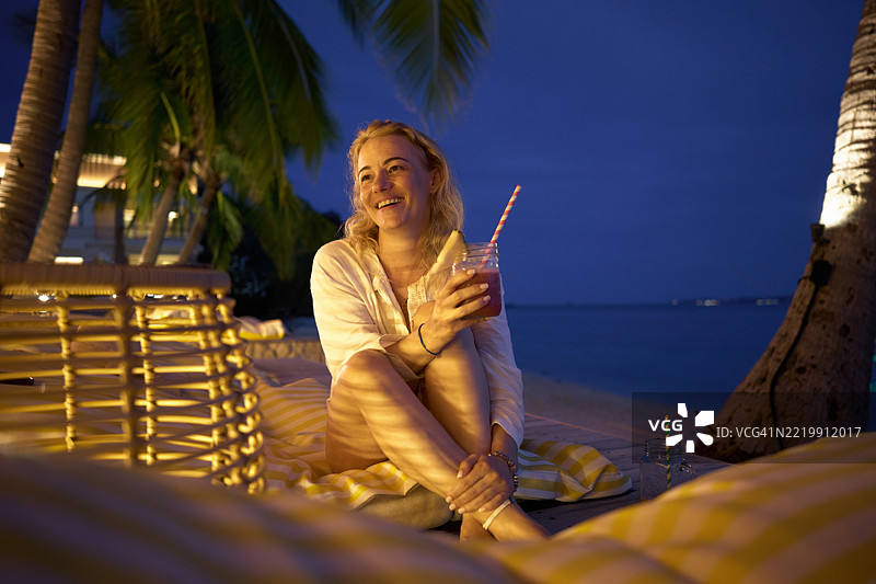 快乐的女人在海滩上夜晚享受饮品。图片素材