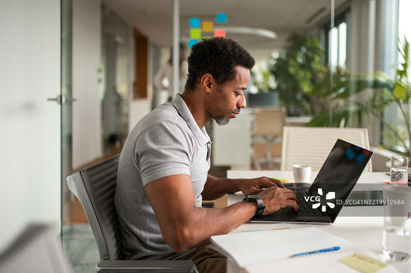 专注的黑人商务专业人士在明亮现代的会议室中使用笔记本电脑图片素材