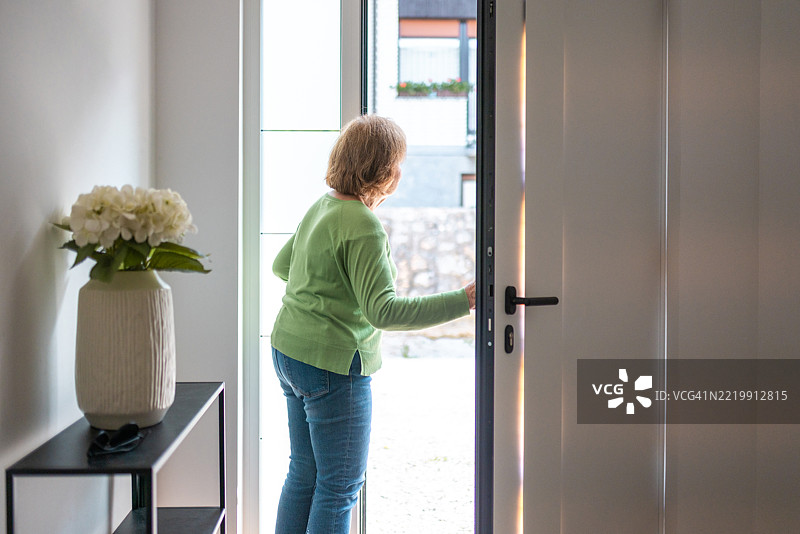 穿着绿色毛衣的老年女性正在打开现代家居的门图片素材
