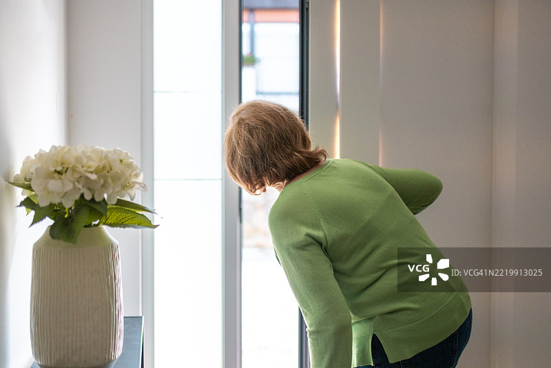 穿着绿色毛衣的老年女性在明亮的自然光中望向家门口图片素材