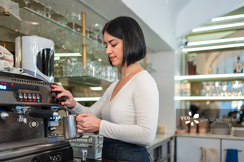 年轻女性咖啡师在现代咖啡馆环境中用咖啡机打奶泡图片素材