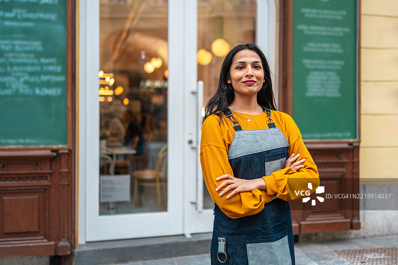 穿着黄色毛衣的中年亚洲咖啡师自信地站在咖啡馆门口图片素材