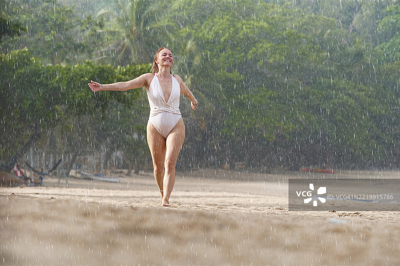 快乐的女人在海滩上享受雨天的乐趣。图片素材