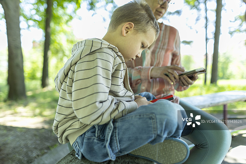 代际科技对比：小男孩正在玩复古游戏机，而他的祖母则拿着一部现代智能手机。图片素材