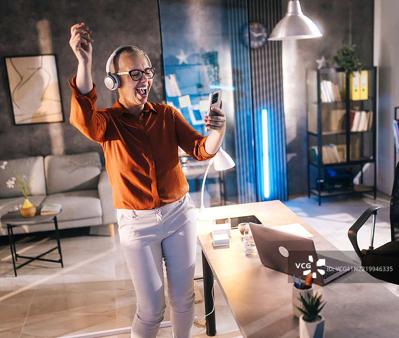 在办公室内，戴着耳机的快乐女性肖像，表现出兴奋的情绪。图片素材