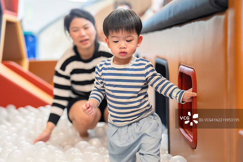 一个顽皮的两岁男孩在室内游乐场享受滑入五彩斑斓的球池。伴随着灿烂的笑容和愉快的精力，这个幼儿在色彩缤纷的环境中探索，创造出快乐的主动游戏和感官学习时刻。图片素材