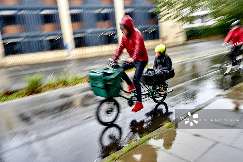 一位女性骑自行车者和她的孩子在雨中骑行。伦敦，英格兰，英国图片素材