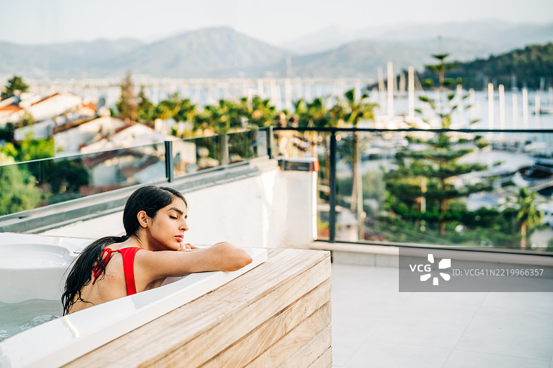 愉快的女性在日落时分的户外浴缸中放松。图片素材