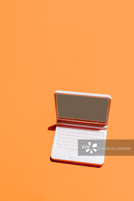 白色笔记本电脑放在橙色背景上，屏幕空白，什么都没有显示。图片素材