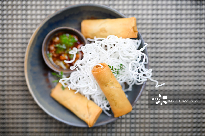 平铺的春卷，配有蘸酱和灰色碗中的米粉，放在有纹理的餐垫上图片素材