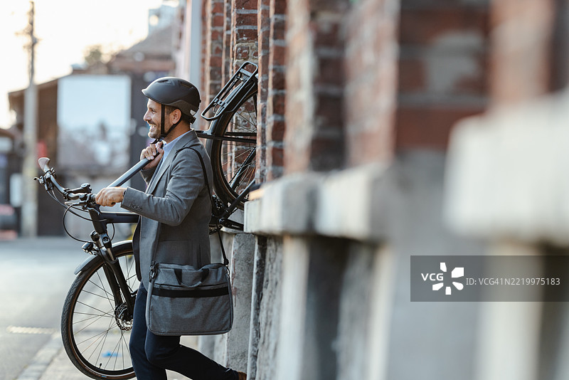 穿着西装的专业男士在户外手持自行车，戴着头盔。图片素材