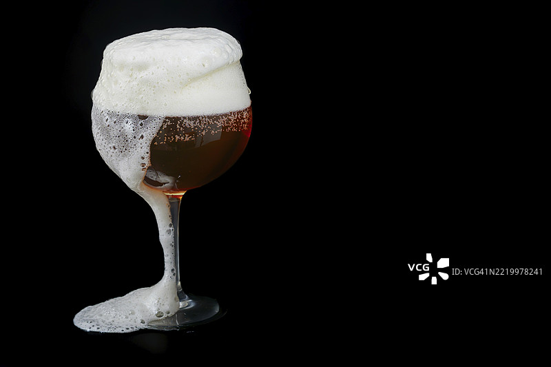 啤酒从玻璃杯中溢出，泡沫丰富，背景为黑色图片素材
