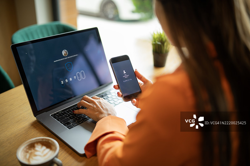 亚洲女性通过输入手机上的代码来验证身份，以登录她的笔记本电脑。图片素材