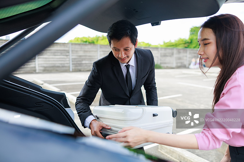 一位礼貌的男性酒店工作人员在酒店停车区为一位女性旅客提供行李协助，突显个性化服务、专业精神和奢华酒店的支持。图片素材