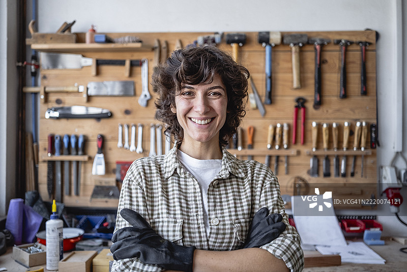 年轻女性木匠自信地站在工作室，背景是工具墙图片素材