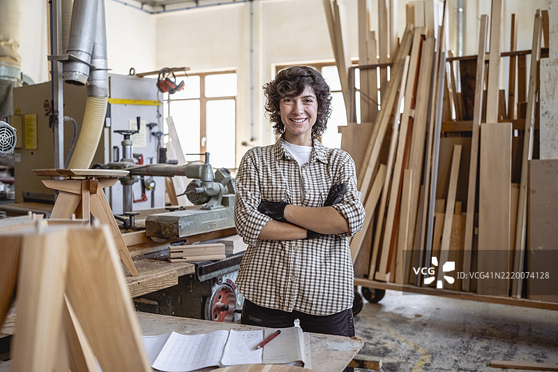 自信的女性木匠站在定制木工车间，周围是工具和材料图片素材