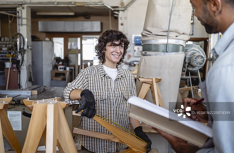 多元化的木匠在光线充足的工作坊中讨论木工项目，使用定制的家具工具图片素材