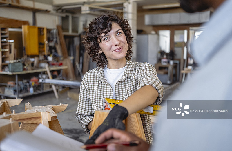 微笑的女性木匠在明亮的工作室里与同事讨论设计方案图片素材