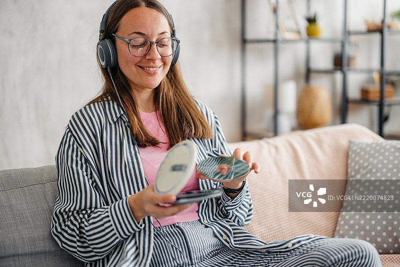 年轻女性坐在沙发上，将CD放入便携式CD播放器中，身处客厅。图片素材