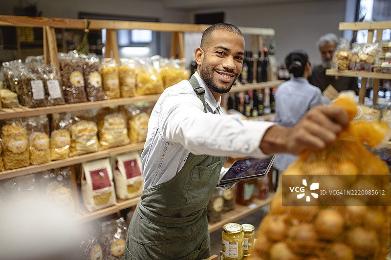 微笑的多种族男性员工穿着绿色围裙，在杂货店整理新鲜农产品图片素材