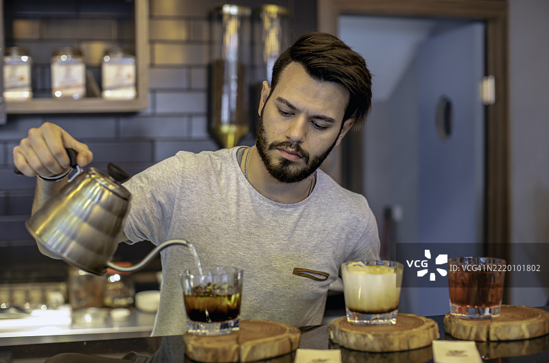 年轻的有胡子的调酒师在现代咖啡馆的吧台后调制色彩缤纷的混合饮品图片素材