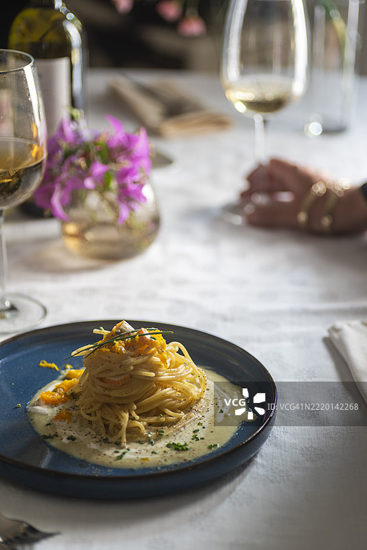 精致的意大利面菜肴和一杯白葡萄酒摆放在优雅的餐桌上图片素材