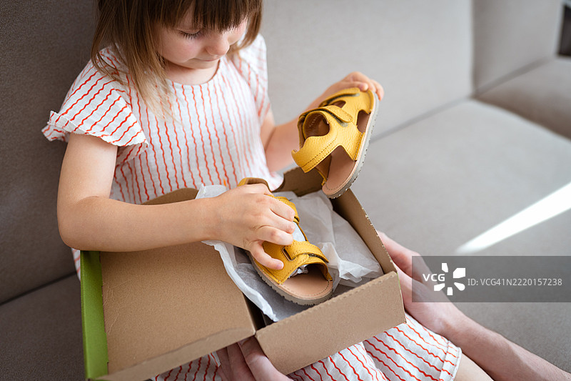 小女孩在沙发上打开一个装有黄色凉鞋的盒子图片素材