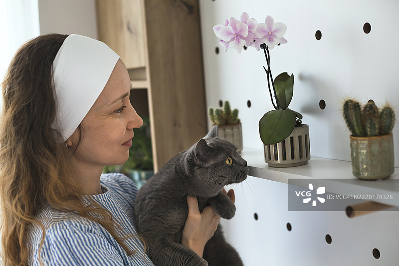 快乐的女人抱着家猫，享受着家中植物的成长。图片素材