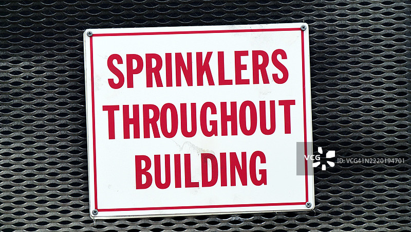 建筑内的喷洒器,写在白色和红色的面板上。工业风格的金属格栅。粗糙的纹理。阳光。自然色彩。美国纽约州皇后区长岛市。图片素材