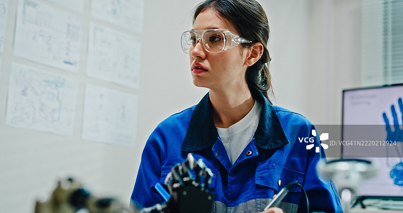 年轻女性工程师在技术实验室使用万用表和焊接工具测试和修理机器人手臂。人工智能与机器人开发。图片素材