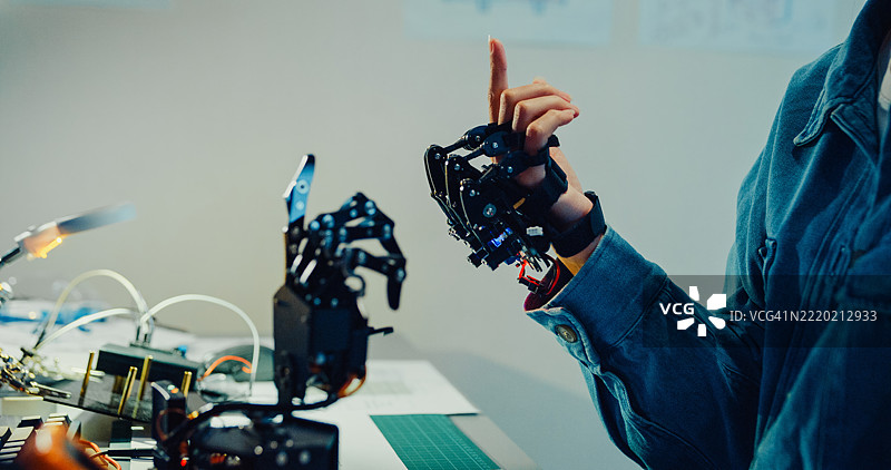 年轻女性工程师在夜间的科技实验室里加班，手势指向机械臂。机器学习、计算机制造、创新与创造力。人工智能与机器人开发。图片素材