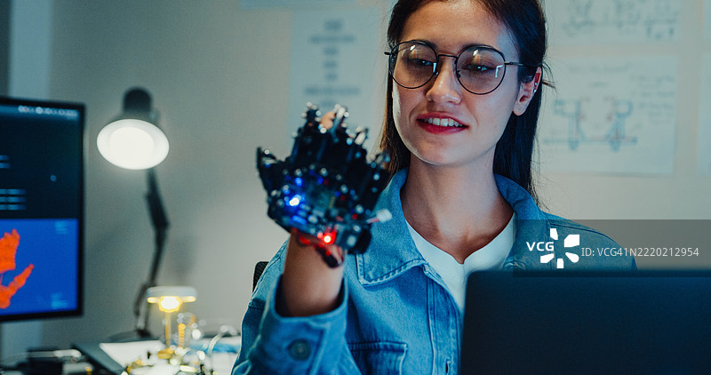 年轻女性工程师在夜间的科技实验室加班，向机器人手臂做手势。机器学习、计算机制造、创新与创造力。人工智能与机器人开发。图片素材