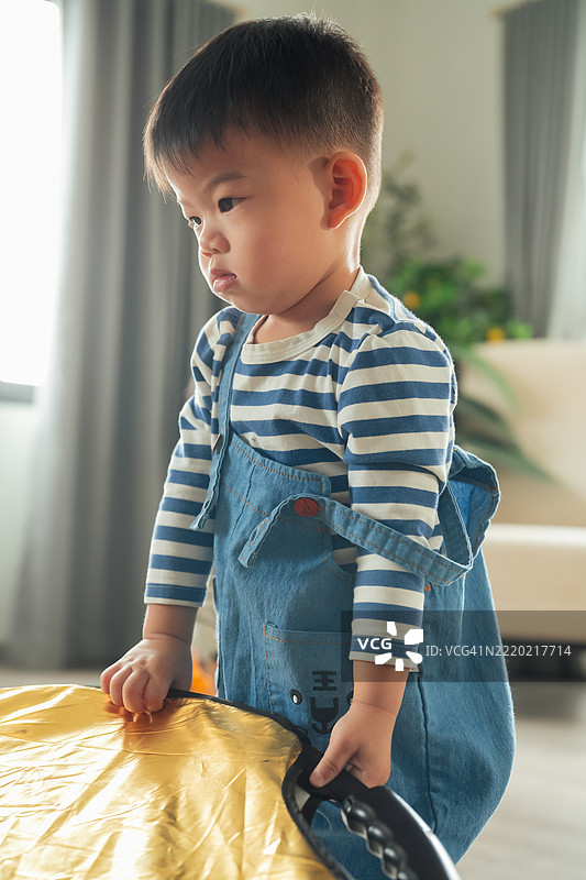 快乐的亚洲男婴学习走路，练习平衡身体，在家居室内背景中迈出第一步，他对周围的一切充满好奇，正在玩耍。图片素材