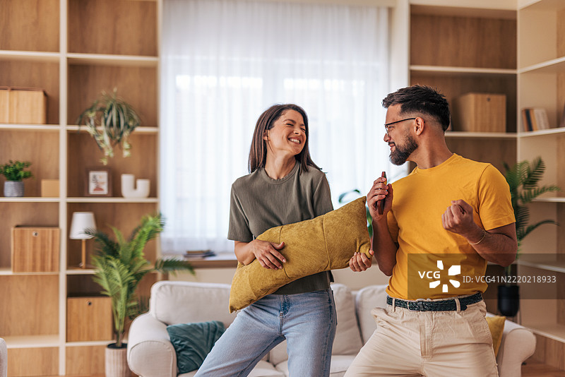 快乐的情侣在家中用智能手机唱卡拉OK并跳舞图片素材