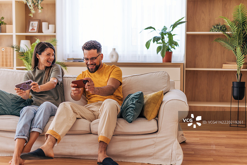 快乐的情侣在沙发上玩手机视频游戏图片素材