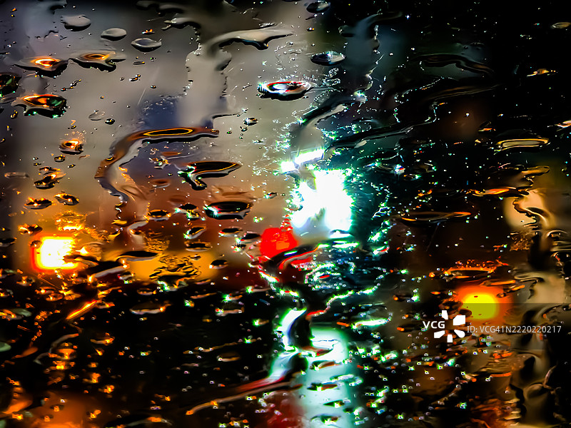 夜晚透过雨水浸湿的玻璃看到的五彩斑斓的城市灯光图片素材