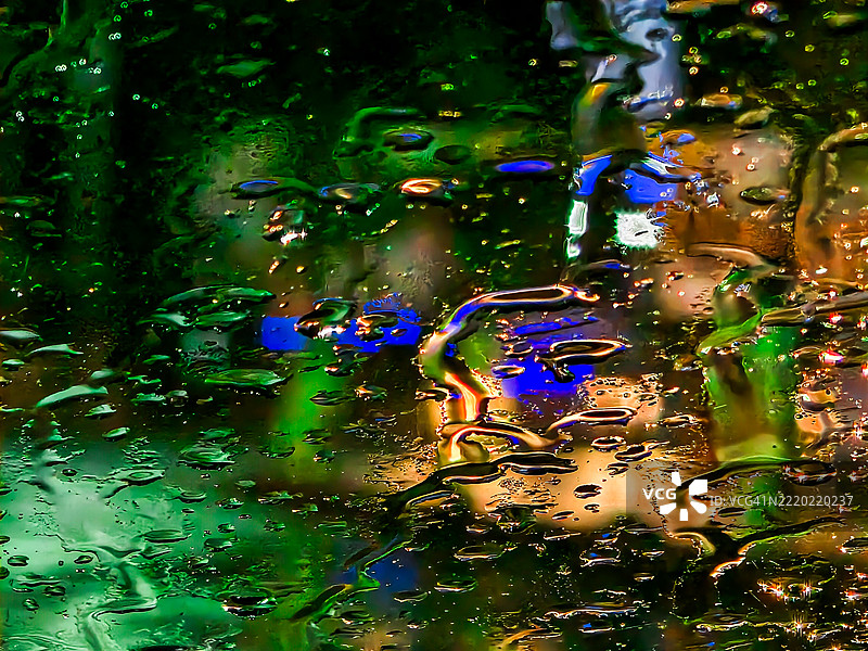 夜晚透过雨水浸湿的玻璃看到的五彩斑斓的城市灯光图片素材