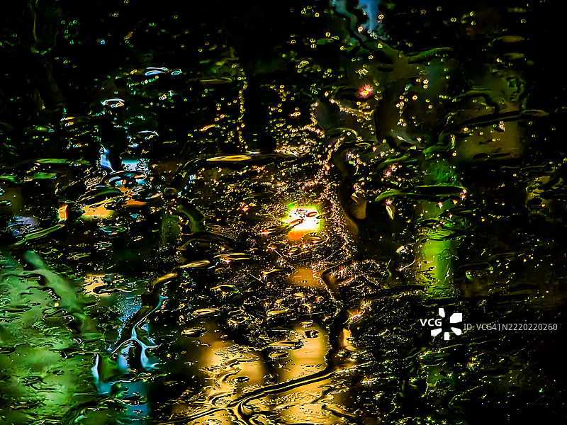 夜晚透过雨水浸湿的玻璃看到的五彩斑斓的城市灯光图片素材