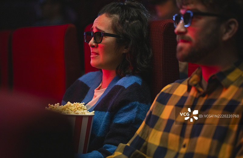 多元化的年轻情侣在昏暗的电影院里享受3D电影和爆米花图片素材