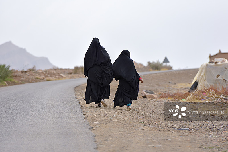 穿着黑色阿巴亚的女性在摩洛哥扎戈拉省德拉河谷的道路上行走图片素材
