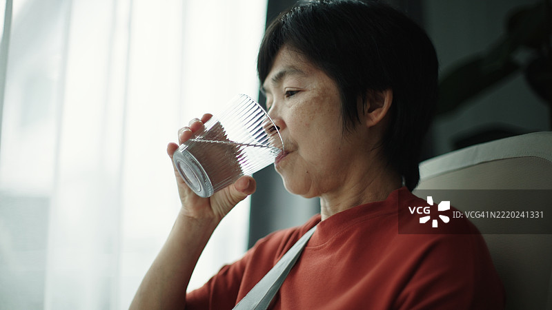 戴着手臂石膏的成熟的女性在喝水。图片素材